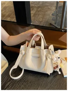 Détail du sac à main en cuir grainé crème avec breloque ours et nœud décoratif.