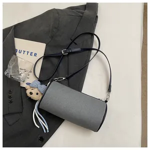 Minimalist gray cylinder crossbody bag with navy blue strap and teddy bear charm.
