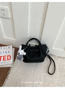 Elegant black textured leather bucket bag with a cute plush dog charm on a white rug