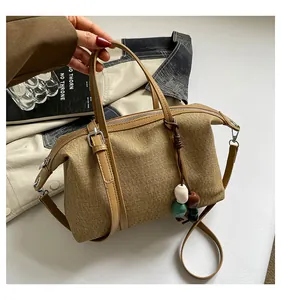 Close-up view of a khaki canvas tote bag with beaded charm and leather shoulder strap