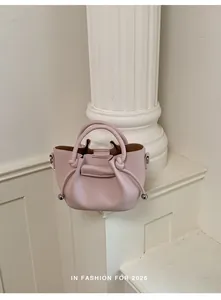 Detailed view of a pale pink leather bucket bag with top handles on a white pillar