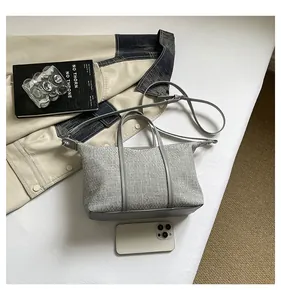 Grey canvas tote bag with leather straps displayed with a phone on a white surface