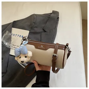 Detail shot of a chic beige canvas cylinder crossbody bag with a cute bear charm