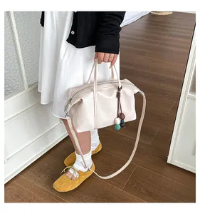 Detailed view of a cream canvas handbag with a colorful bead charm carried by a model