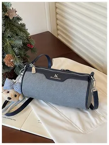 Detail view of a stylish grey barrel crossbody bag with denim texture and bear charm.