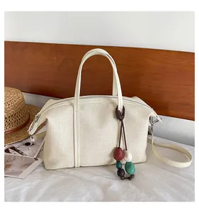 Close-up of a cream-colored canvas tote bag with a colorful bead charm on a white bed