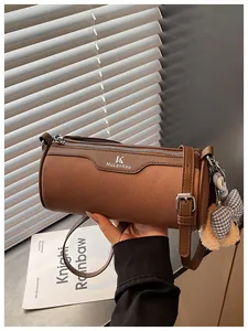 Close-up of a stylish brown cylinder crossbody bag with a cute bear charm accessory