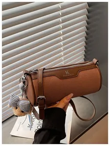 Detailed view of a brown canvas barrel crossbody bag featuring a cute teddy bear charm.
