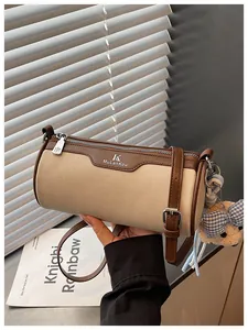 Detail view of a handheld cylindrical canvas and leather barrel bag with bear charm