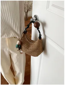Gros plan d'un sac à bandoulière en paille tressée avec bandoulière en cuir et perle en bois