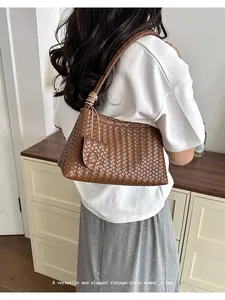 Model wearing a brown woven leather underarm bag with elegant vintage-style details