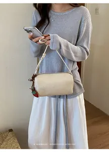 Detailed view of a minimalist cream white pillow bag with a strawberry charm accessory
