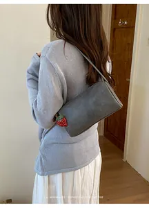 Back view of a minimalist grey pillow bag with a strawberry charm on a shoulder.
