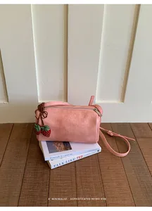 Detail view of pink minimalist pillow bag with strawberry charms on vintage books backdrop