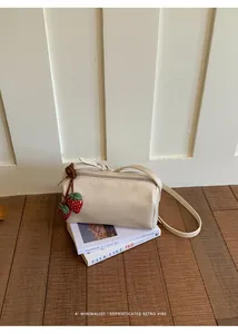 Minimalist cream cylinder shoulder bag with cute strawberry charm on wooden floor