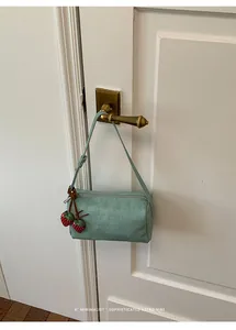 Mint green suede barrel bag with strawberry charm hanging on a vintage door handle.