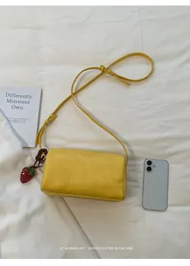 Minimalist yellow pillow bag with cute strawberry charm accessory on white textured background