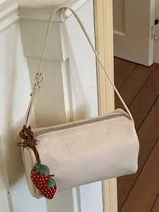 Chic minimalist beige cylindrical pillow bag with a cute decorative strawberry charm