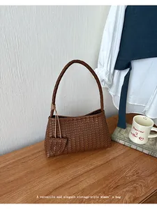 Elegant brown woven leather underarm bag on wooden table with vintage style props