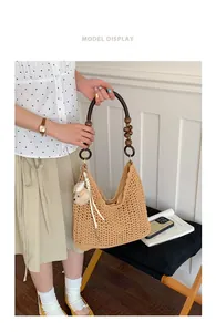 Detailed view of a woman holding a stylish khaki straw woven shoulder bag for beach trips