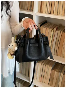 Sac à main en cuir grainé noir devant un fond d'étagères blanches remplies