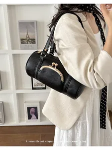 Elegant black vintage-style cylinder shoulder bag carried by a woman in a chic outfit