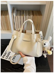 Vue détaillée d'un sac cabas en cuir texturé crème tenu à la main avec un ours