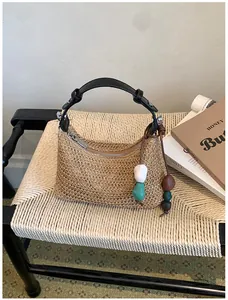 Détail du sac à main en paille tressée avec poignée noire et breloque perlée