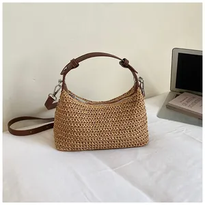 Détail d'un sac à main en paille tressée avec lanières en cuir marron sur un bureau blanc