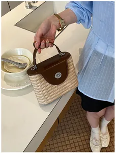 Gros plan détaillé d'un sac seau en paille fait main avec rabat en cuir marron à la main.
