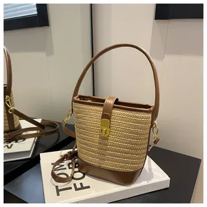 Primo piano della borsa a secchiello in paglia intrecciata a mano con finiture e fibbia dorata.