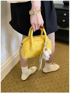 Vibrant yellow Boston bag with cute bear charm held by a model in casual chic outfit.