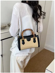 Close-up of a woven straw bag featuring natural bamboo handles and black faux leather accents