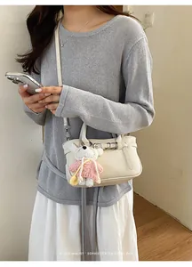 Elegante borsa a tracolla in pelle crema indossata da una donna con un simpatico ciondolo a orso