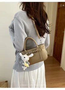 Dettaglio di una borsa in pelle kaki con ciondolo di peluche su maglione grigio