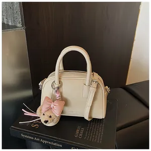 Elegant cream mini pillow handbag on a black book prop with a cute bear charm.