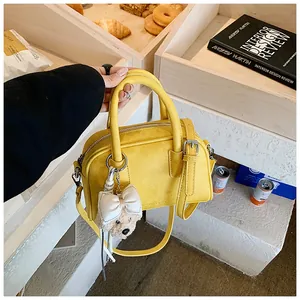 Detail shot of yellow suede pillow bag with plush bear charm in a cafe setting
