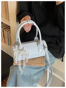 Detail view of a light blue barrel bag with a pearl bow charm and lace ribbon.