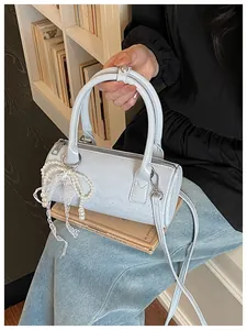 Detail view of a light blue cylindrical barrel bag with pearl and lace bow accessory