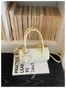 Elegant cream barrel handbag with decorative pearl lace bow shown on a vintage bookshelf