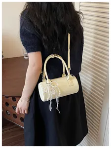 Elegant cream cylindrical women's crossbody bag featuring a pearl bow charm detail