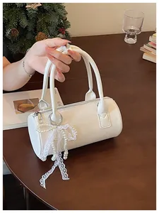 Close-up view of a white cylindrical handbag with elegant pearl and lace bow charm detail