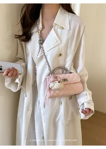 Detail of a pink quilted crossbody handbag with a plush charm on a model in a white coat.