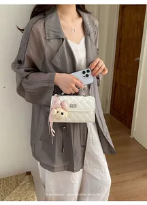 Close-up of white quilted handbag with cute teddy bear charm held by woman