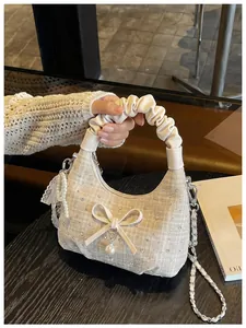 Gros plan d'un sac à main en tweed crème avec poignée plissée, nœud et pendentif perle