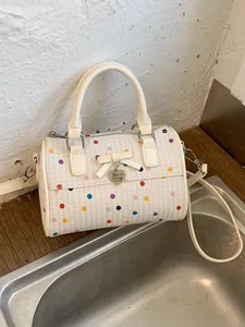 Elegante bolso de mano crema con lunares, detalle de lazo y colgante de corazón