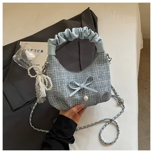 Détail du sac à main en tweed bleu avec froufrous, nœud et breloque en perle.