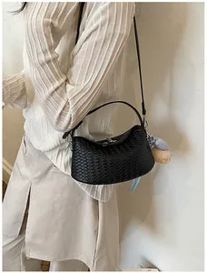 Close-up detail shot of a black woven crossbody bag styled with a white ribbed sweater outfit.