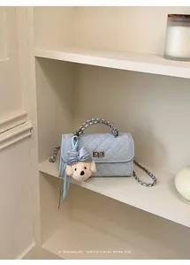 Elegant light blue quilted mini crossbody bag with teddy bear charm on minimalist shelf