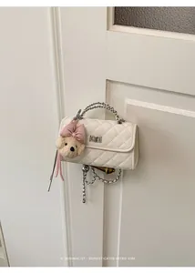 Close-up of white quilted mini bag with plush teddy bear charm on door handle